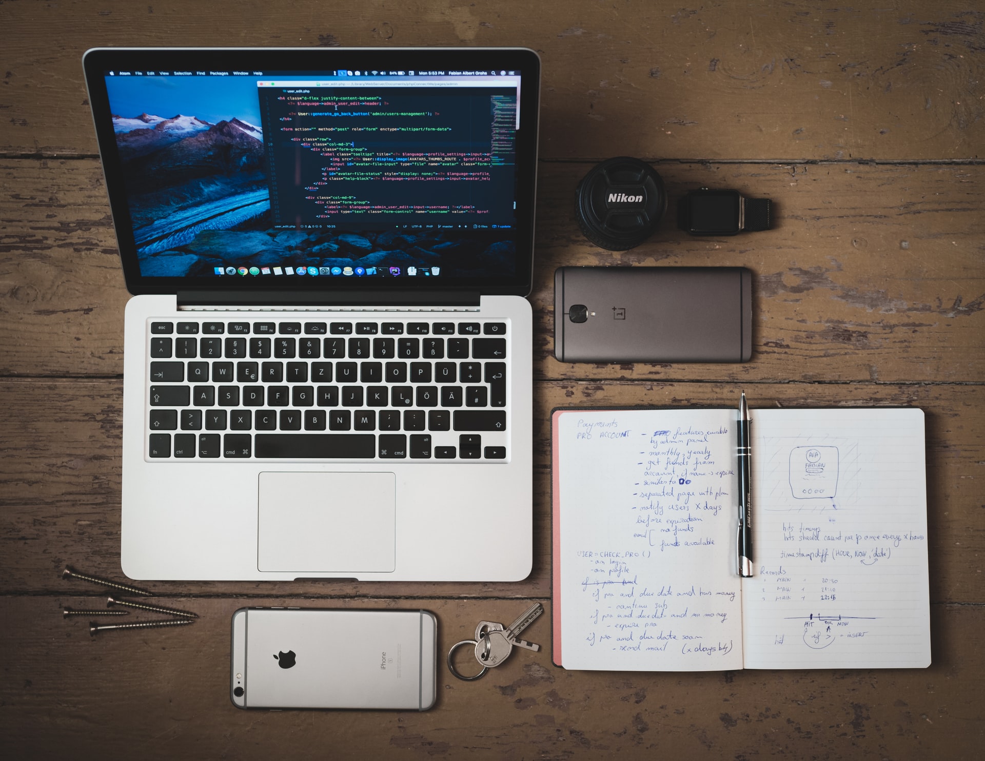 Laptop, notepad, two phones and other items on a wooden table